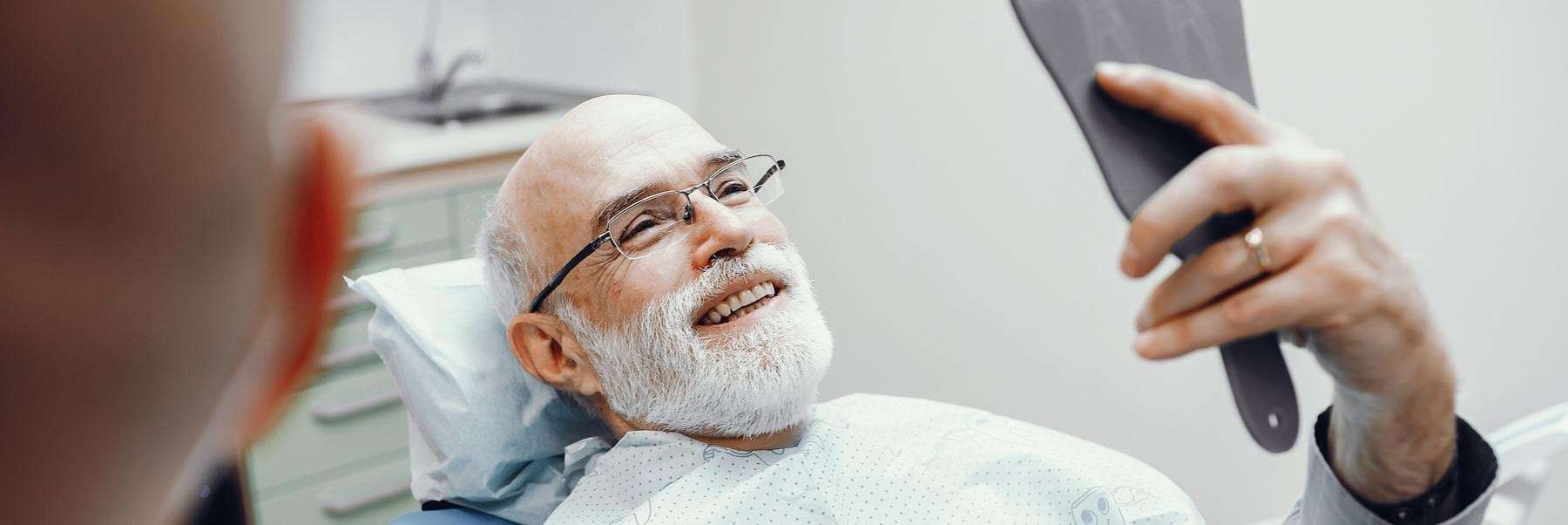 old man in dental chair holding mirror